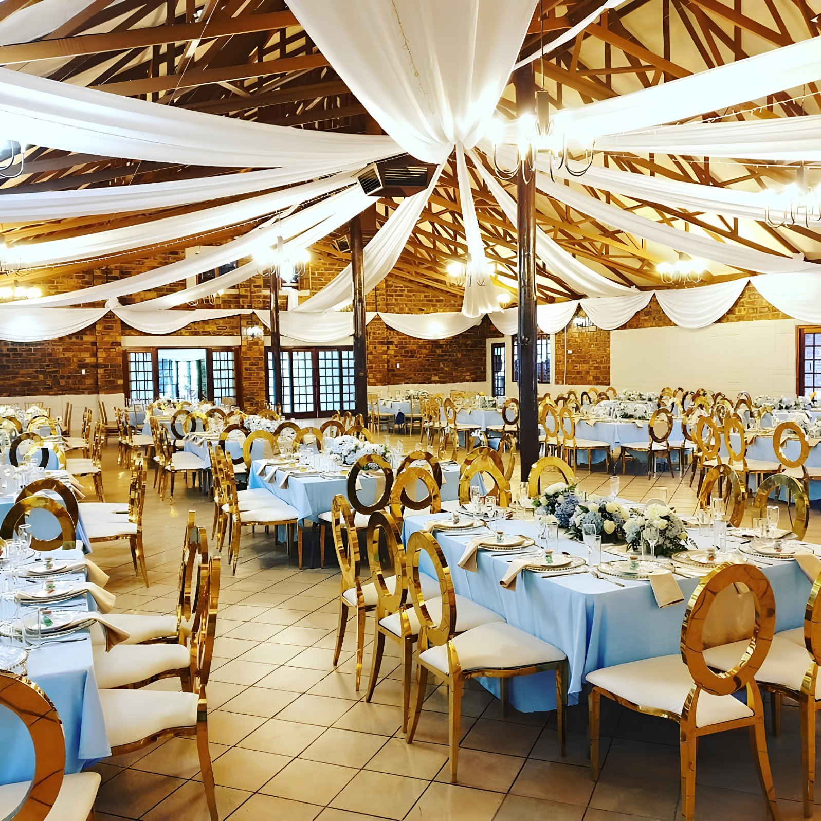 The hall at The Pines dressed for a function: white draping under the timber roof, chandeliers, blue tablecloths and gold chairs