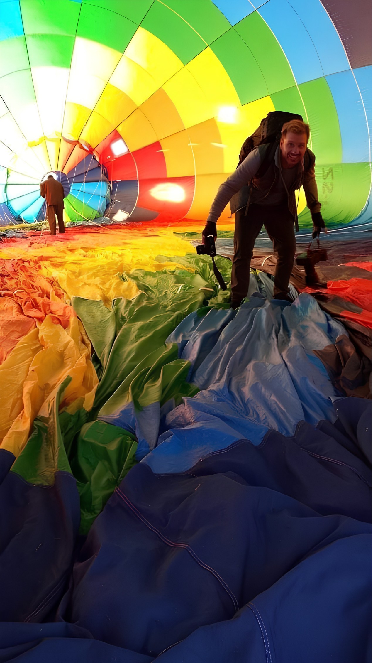A photographer grinning inside a rainbow hot-air balloon as it is laid out and inflated on the grass