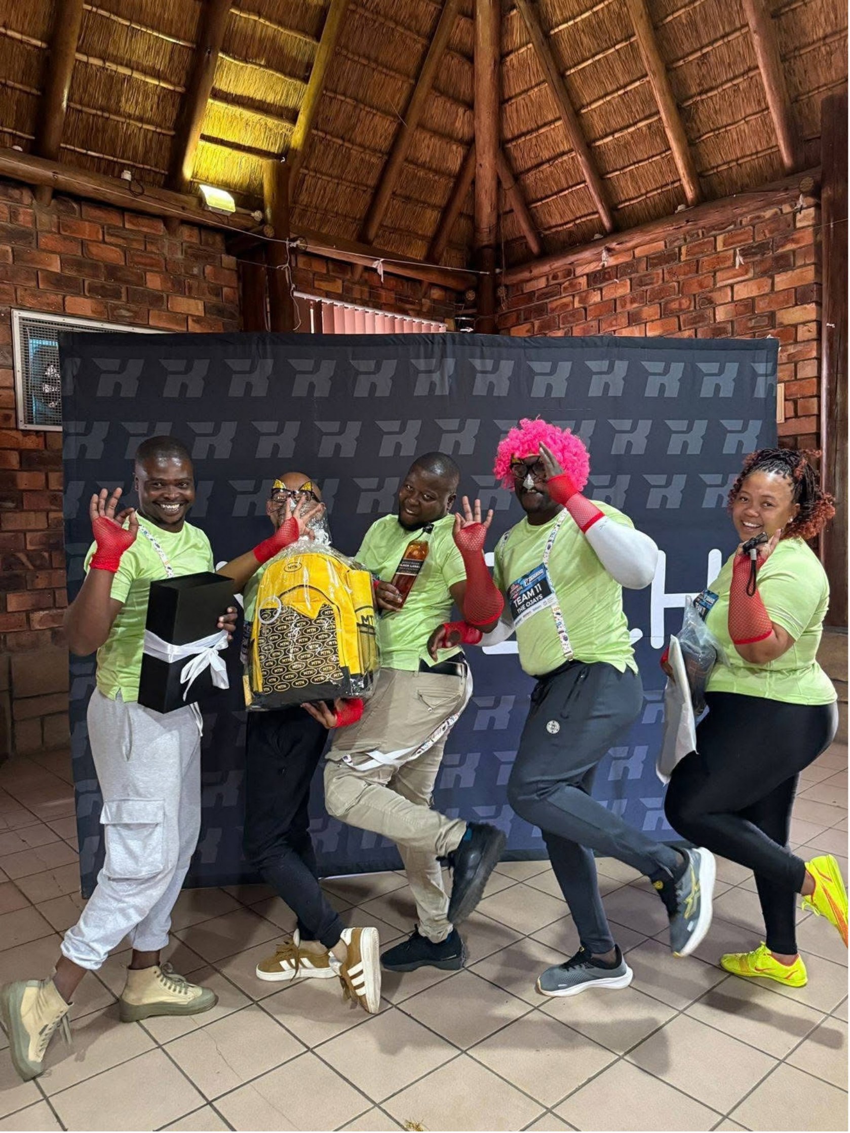 A Lekker Resies team in pink wigs and red gloves strikes a pose in front of the race backdrop