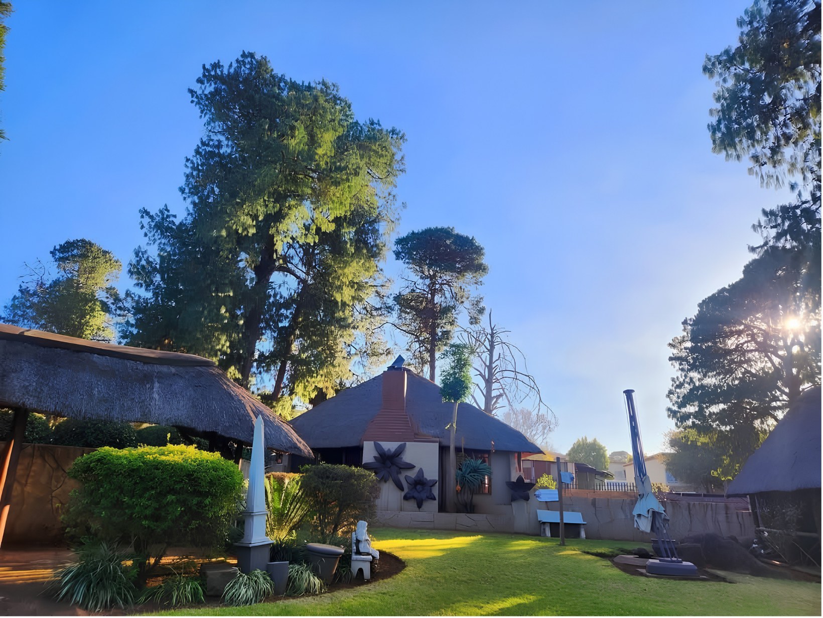 Thatched buildings and a clipped garden on the lawns at The Pines, on a clear day