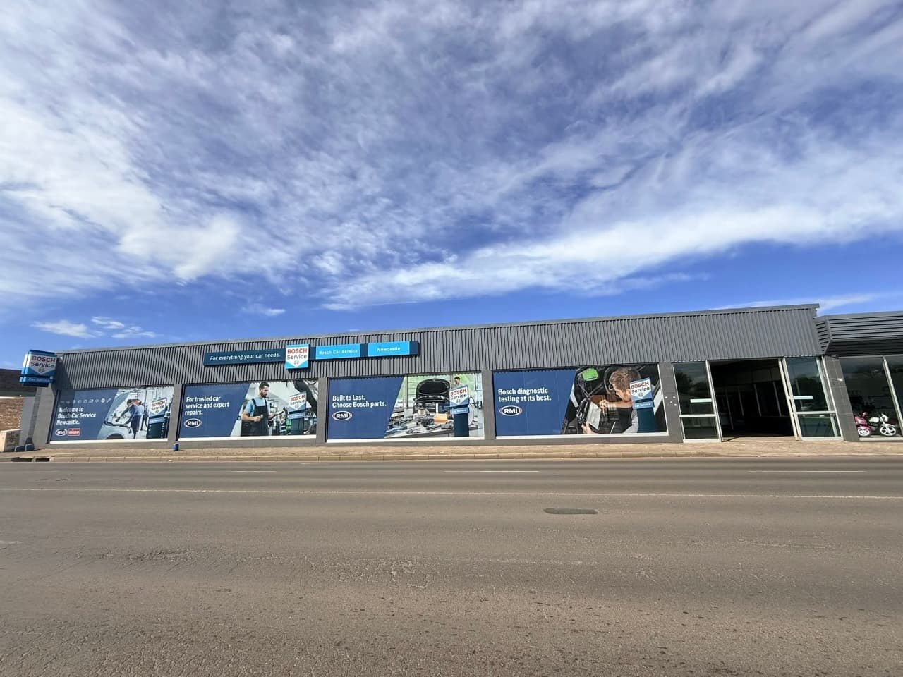The Bosch Car Service building in Newcastle under a wide blue sky, its windows covered in large printed graphics